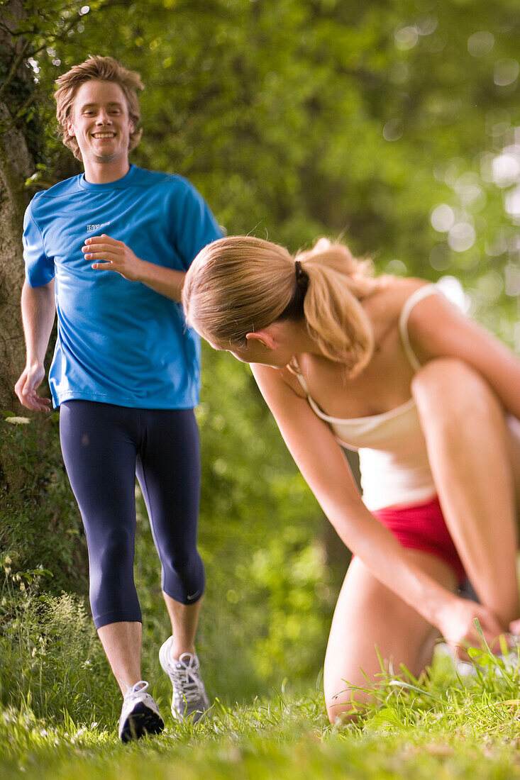 Female jogger tying lace, young man in Background