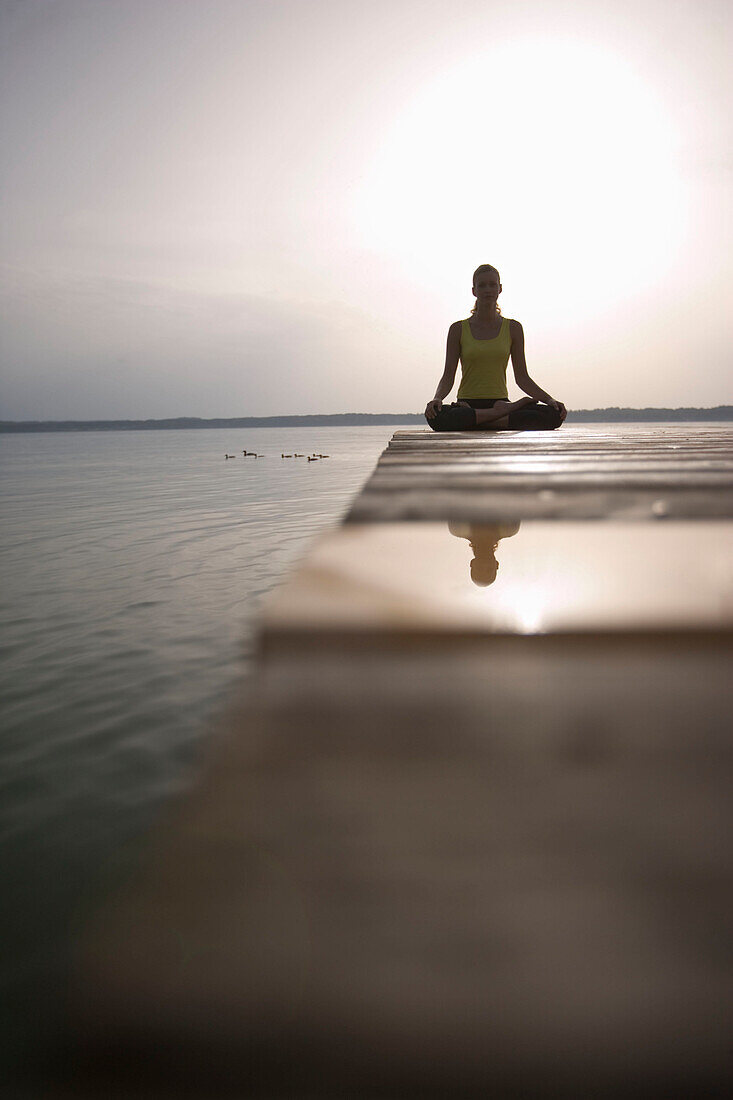 Junge Frau meditiert auf einem Holzsteg am See