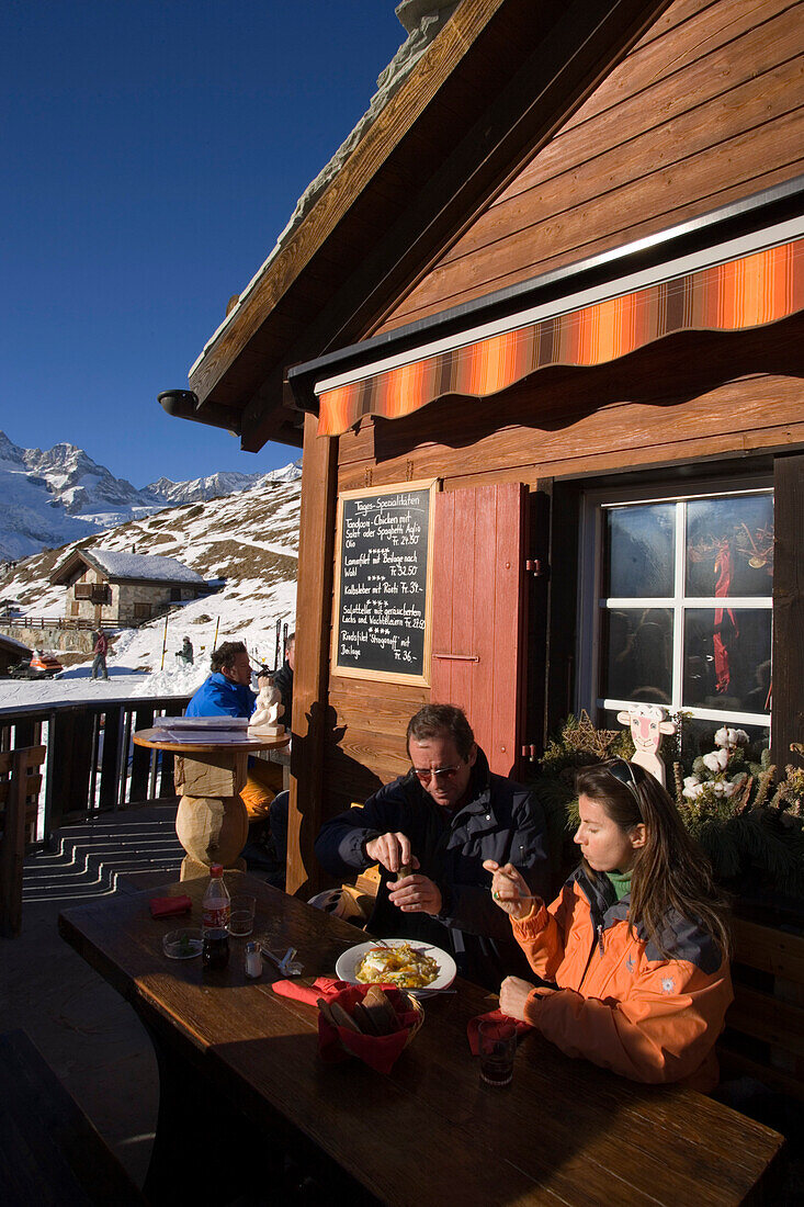 Couple sitting on terrace of Restaurant Paradies (2540 m) and eating, Findeln, Zermatt, Valais, Switzerland