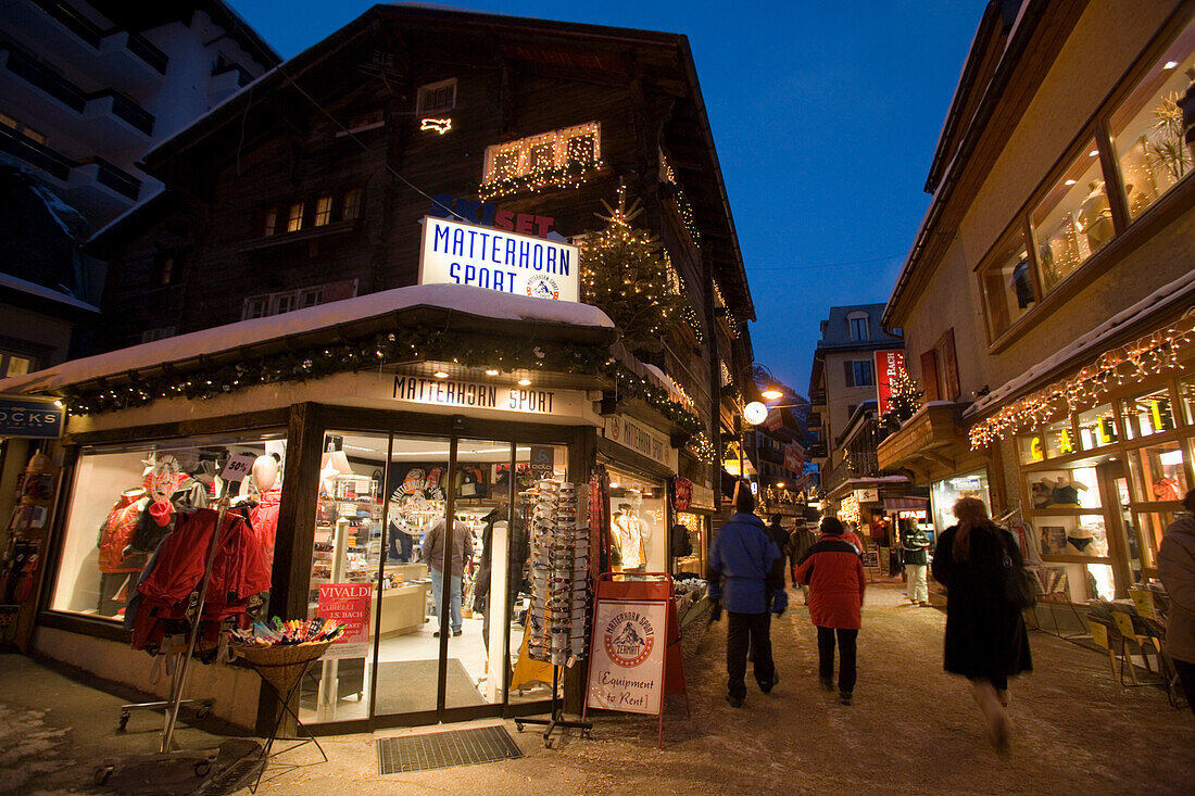 People walking over the shopping street Bahnhofstrasse in the late evening, a sports outfitters in foreground, Zermatt, Valais, Switzerland