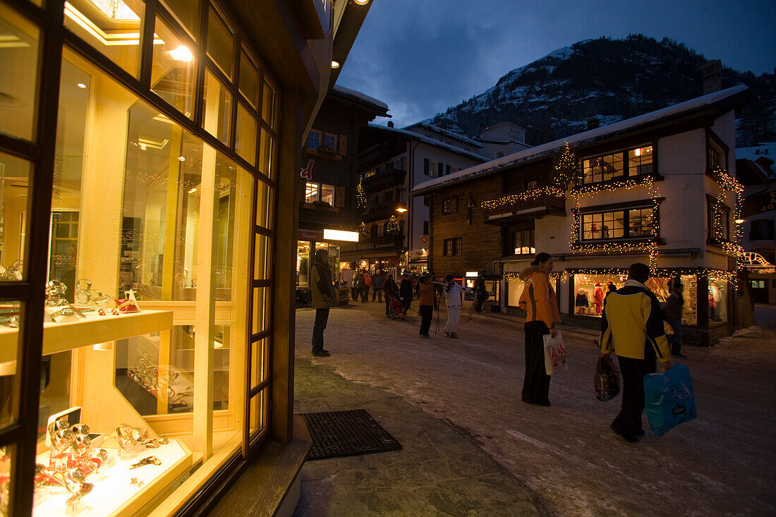 People walking over the illuminated shopping street Bahnhofstrasse in the late evening, Zermatt, Valais, Switzerland