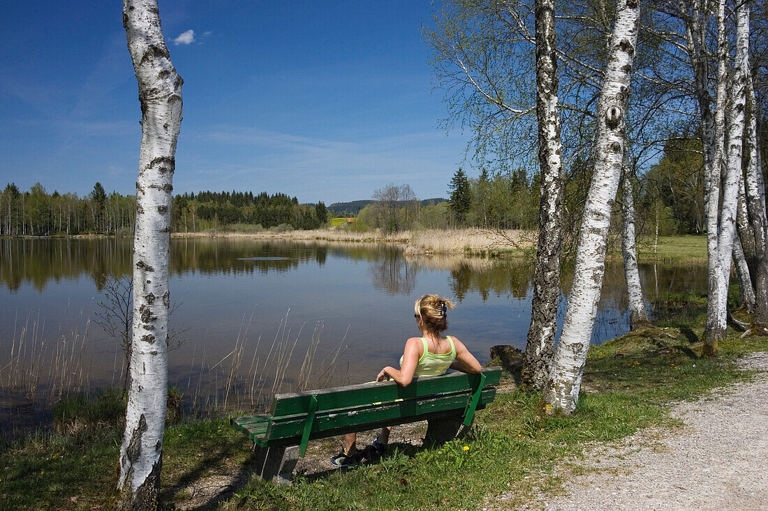 Frau sitzt auf Bank am Bayersoiener See, Oberbayern, Deutschland
