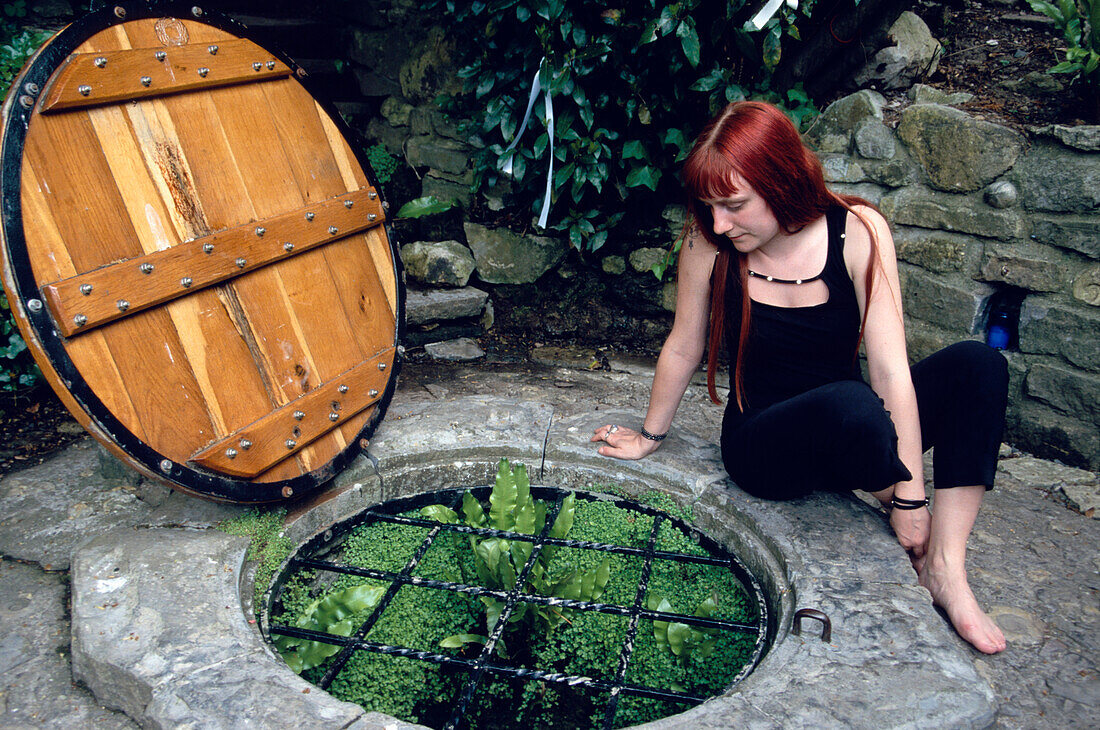Girl sitting next to the famous Chalice Well in Glastonbury related to the King Arthur legend, Somerset, England