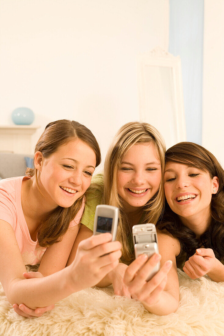 Teenage girls (14-16) on bed using mobil phones
