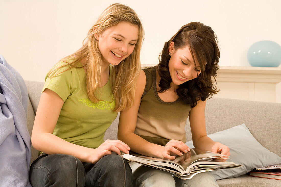 Teenage girls (14-16) sitting on sofa, looking into book