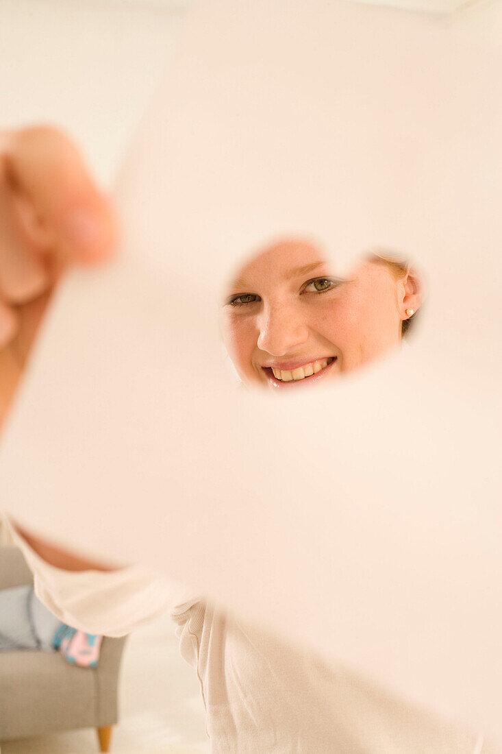 Teenage girl (14-16) holding sheet with hearts in front of face