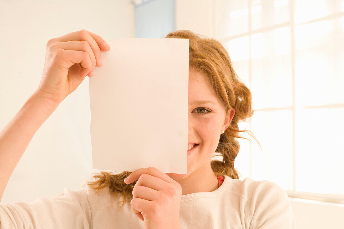 Weiblicher Teenager (14-16) bedeckt Gesichtshälfte mit Briefbogen