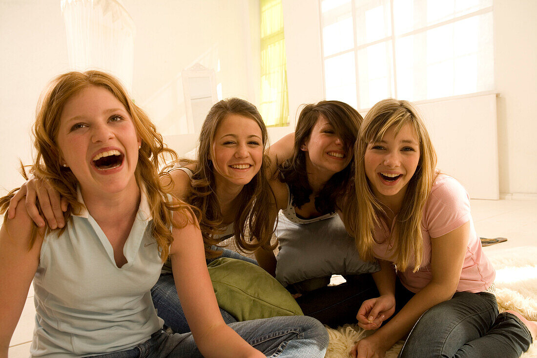 Four teenage girls (14-16) having fun, sitting on floor, indoor