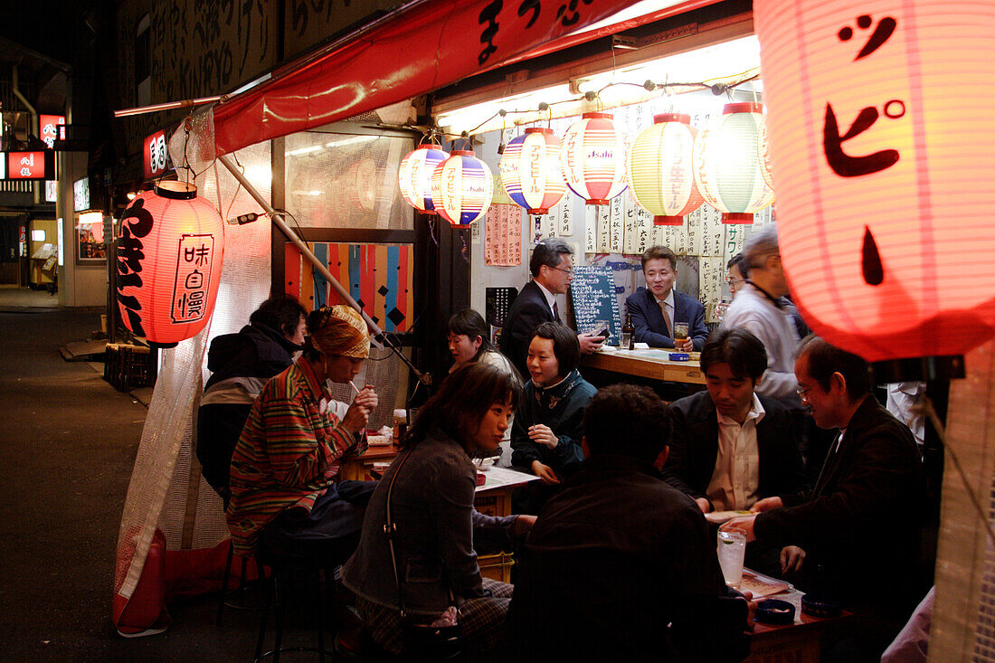 Menschen sitzen nachts vor einem Schnellimbiss, Yurakucho Yakitori Alley, Ginza, Tokio, Japan