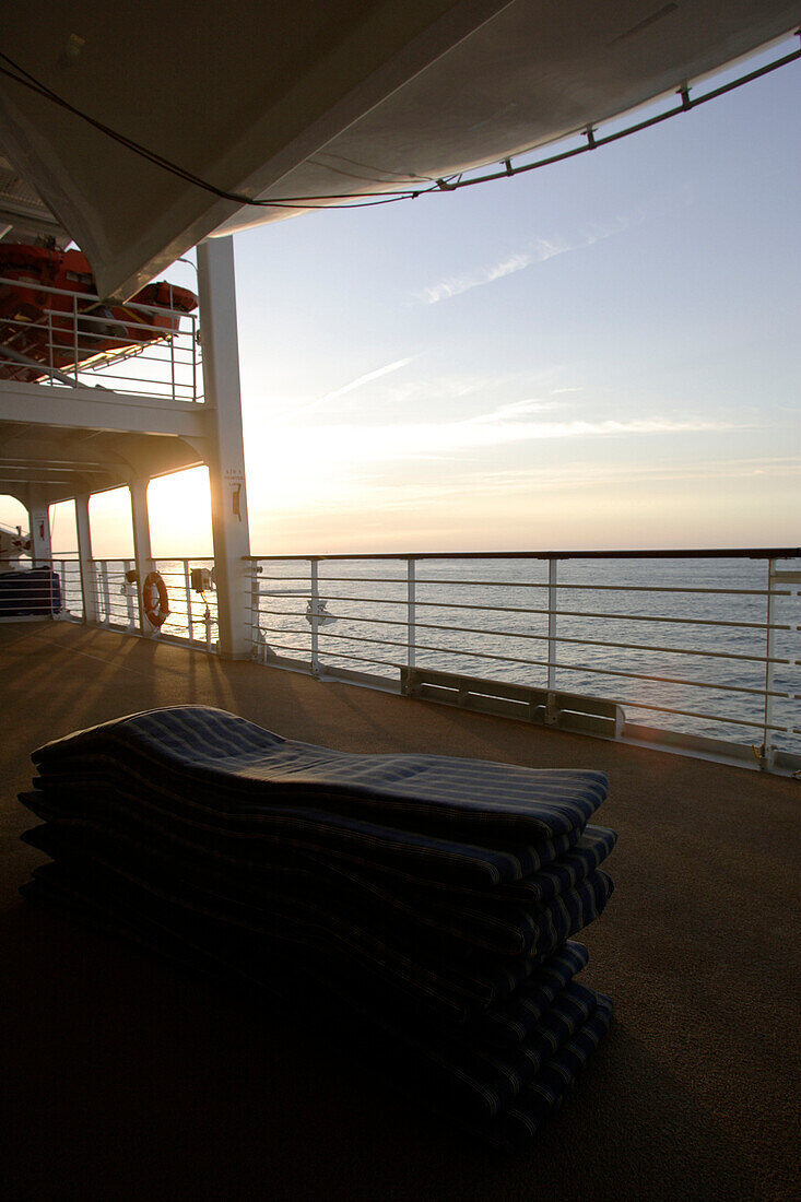 Ein Stapel Polster auf dem menschenleeren Deck bei Sonnenuntergang, Kreuzfahrtschiff MS Delphin Renaissance