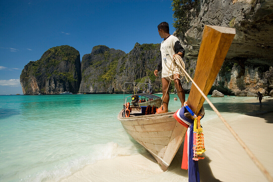 Boatman standing on a long tail boat and holding a rope, Maya Bay, a beautiful scenic lagoon, famous for the Hollywood film "The Beach", Ko Phi-Phi Leh, Ko Phi-Phi Islands, Krabi, Thailand, after the tsunami