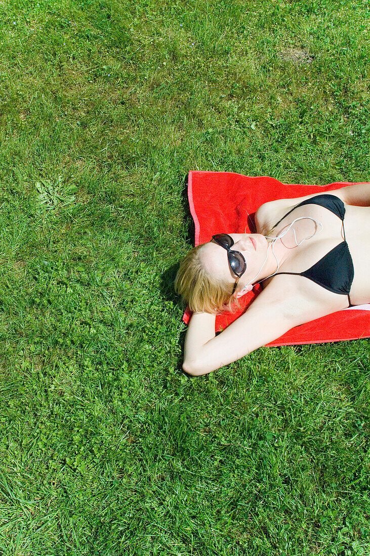 Young woman lying on grass, listening to MP3 player, Starnberger See, Upper Bavaria, Germany