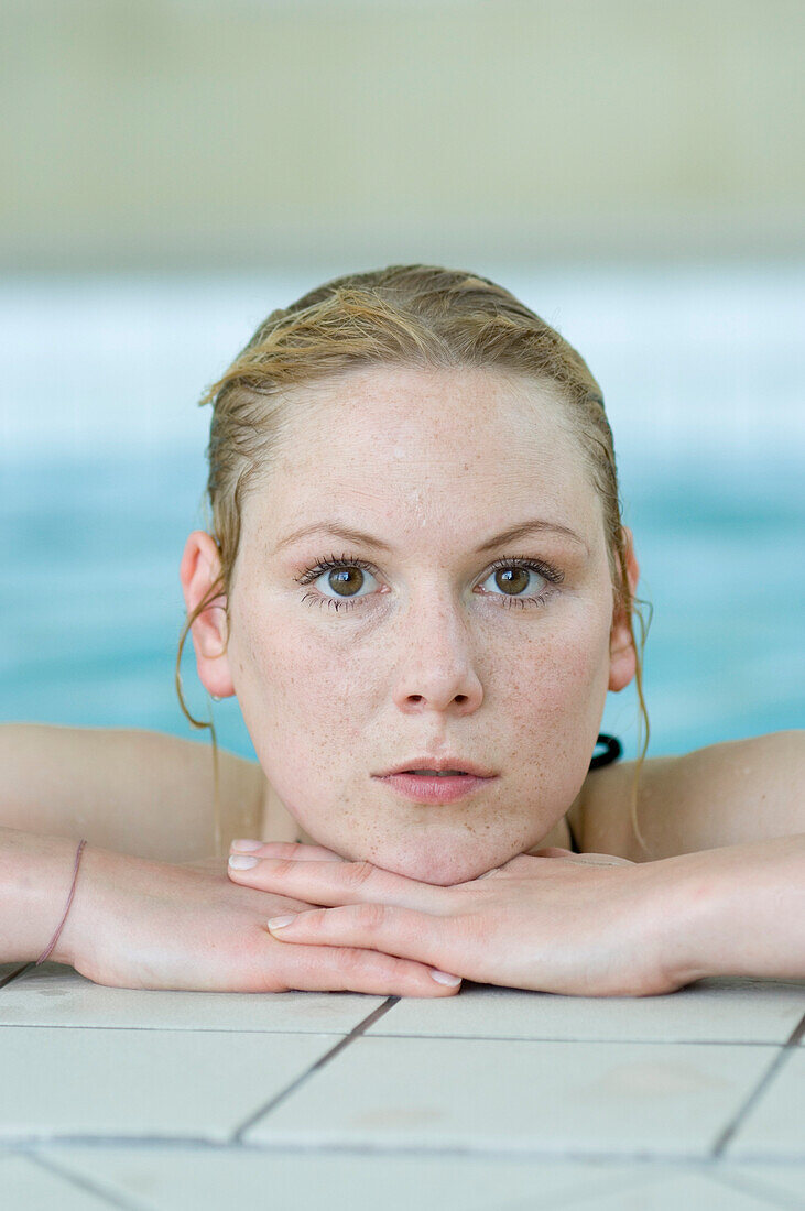 Woman at edge of pool, resting chin on hands, Germany