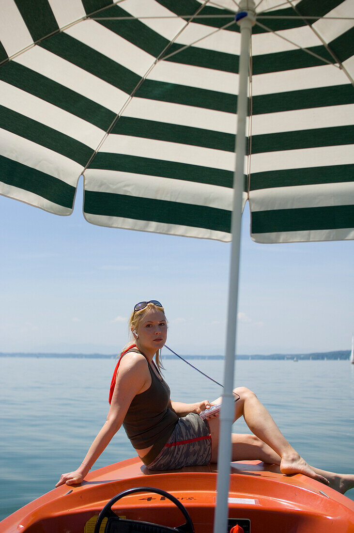 Woman sitting on rental boat with sunshade, listening to MP3 player