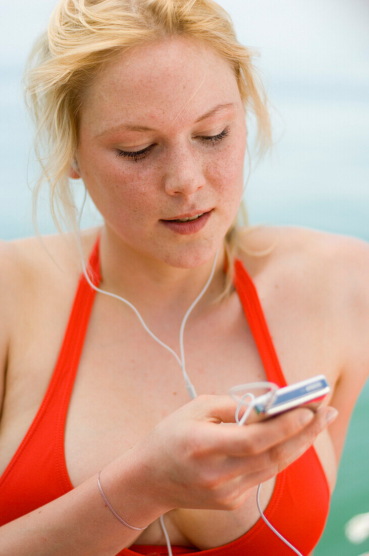 Young woman wearing red bikini top, listening to MP3 player, Starnberger See, Upper Bavaria, Germany
