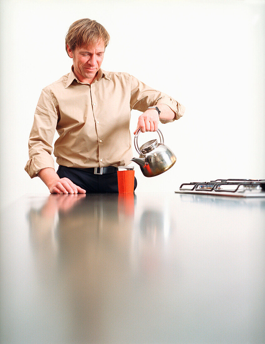 Mann schüttet Wasser in Tasse, Deutscher, Teekanne, eingieþen, einschütten, Getränkewärmer, Küche, Tee trinken