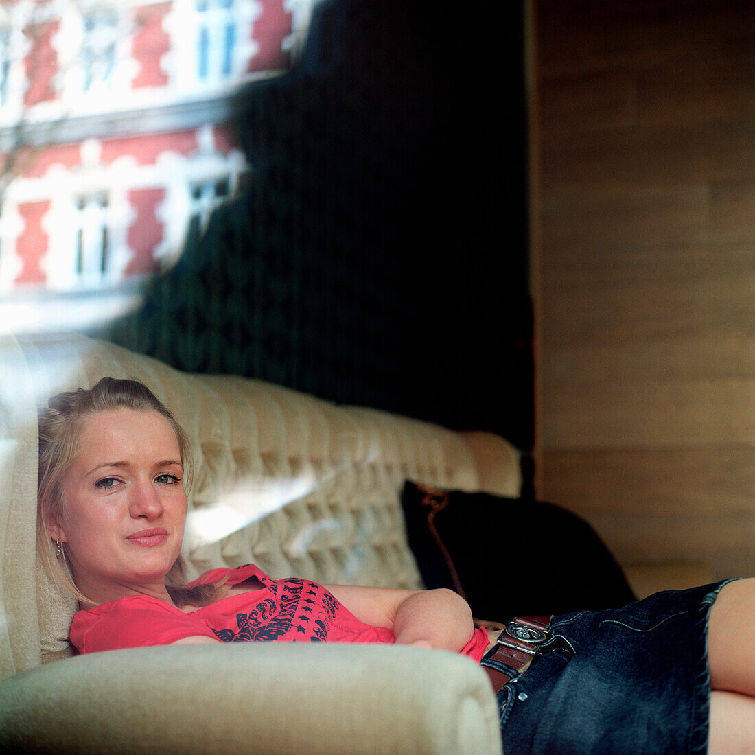 junge Frau auf dem Sofa, Deutsche, blond, kaukasisch, Deutschland, Blick durch Fenster, entspannen, chillen, Freizeit, Blick in die Kamera, Café, Bar, lächeln, stylisch, modern, Szene, anlächeln, rotes Shirt, jeansrock, Spiegelungen in Fensterscheibe