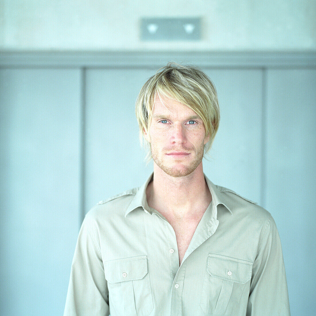 Portrait, blonder Mann, Deutscher, blickt in die Kamera, modern, unrasiert, steht vor Aufzug, blaue Augen