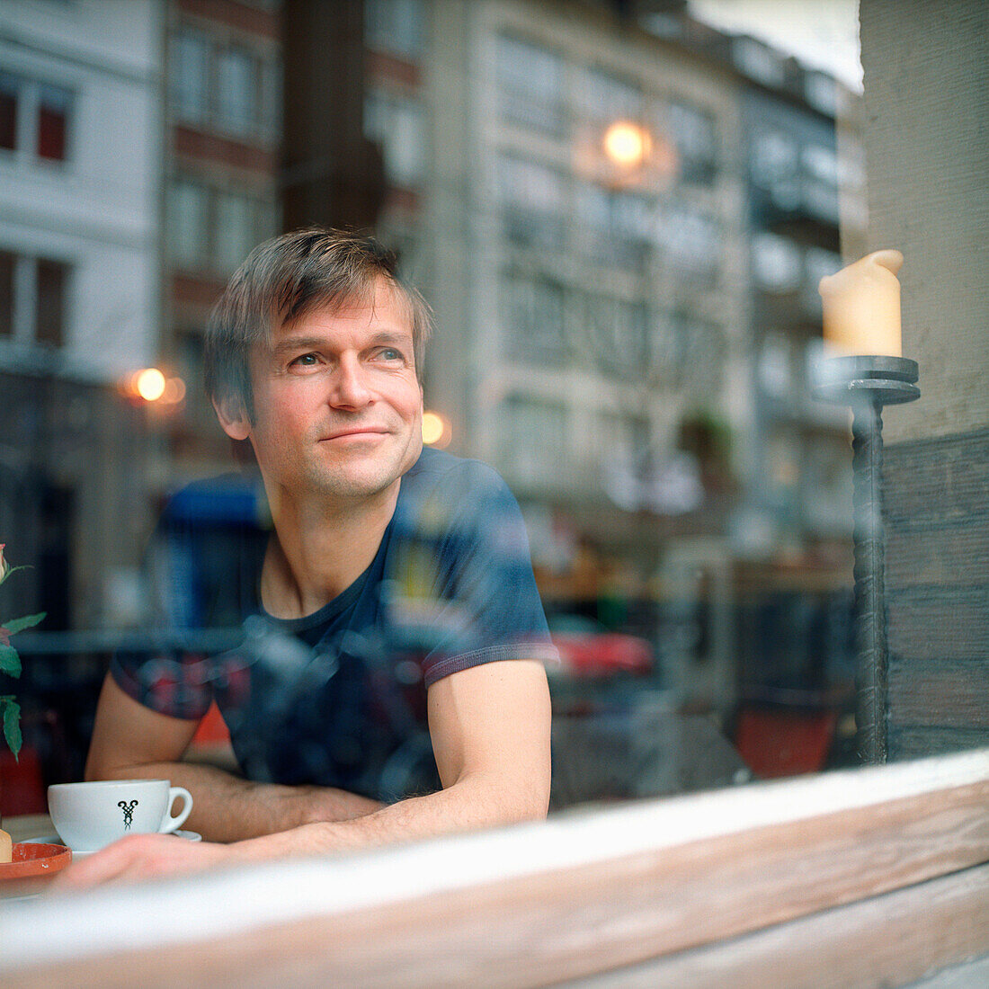 Mann sitzt im Café, Deutscher, Deutschland, Tasse, aus dem Fenster schauen, lächeln, zufrieden, entspannt, in Gedanken, beobachten, Freizeit, genieþen