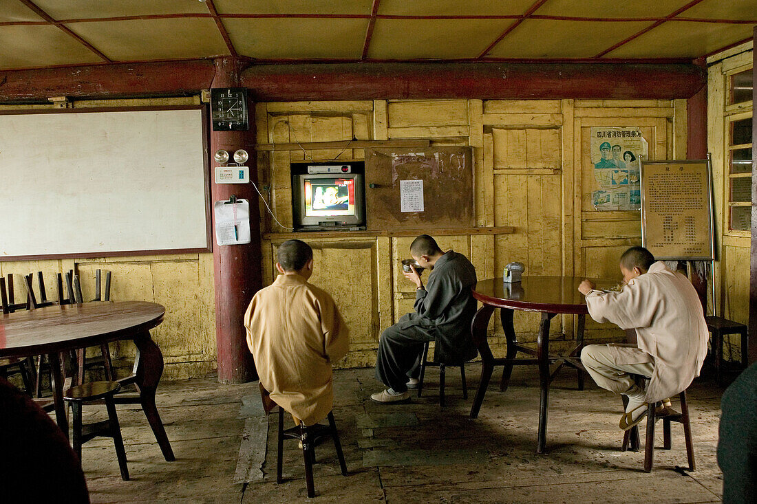 Monks eating at the canteen in front of the television, Xixiang Chi monastery, Emei Shan, Sichuan province, China, Asia