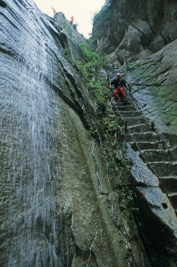 western tourist on steep pilgrim path along stone steps with worn down chain handrail, Hua Shan, Shaanxi province, Taoist mountain, China, Asia