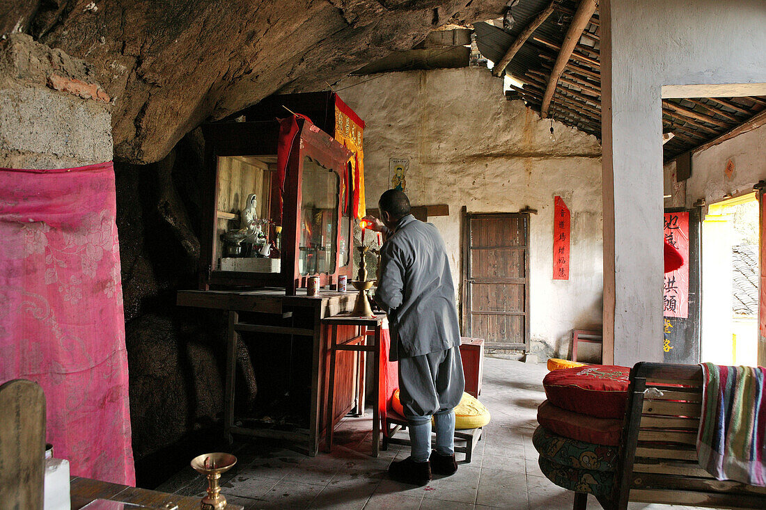 Ein Mönch steht vor dem Alltar eines Höhlentempel, Jiuhuashan, Provinz Anhui, China, Asien