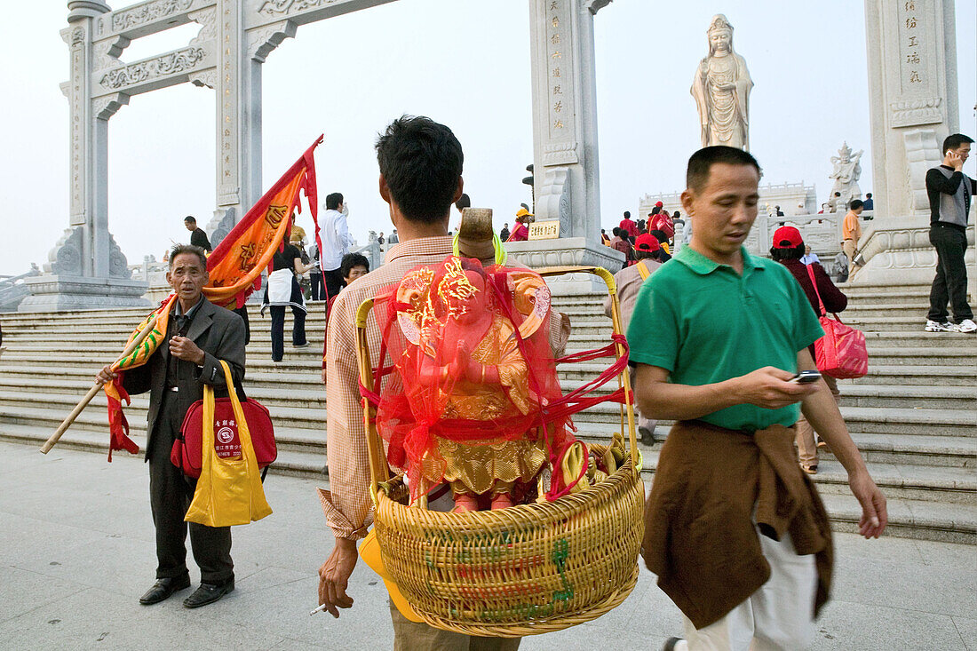 Pilgrim carrying a Buddha statue for a blessing to Guanyin, Goddess of Mercy, Buddhist Island of Putuo Shan near Shanghai, Zhejiang Province, East China Sea, China