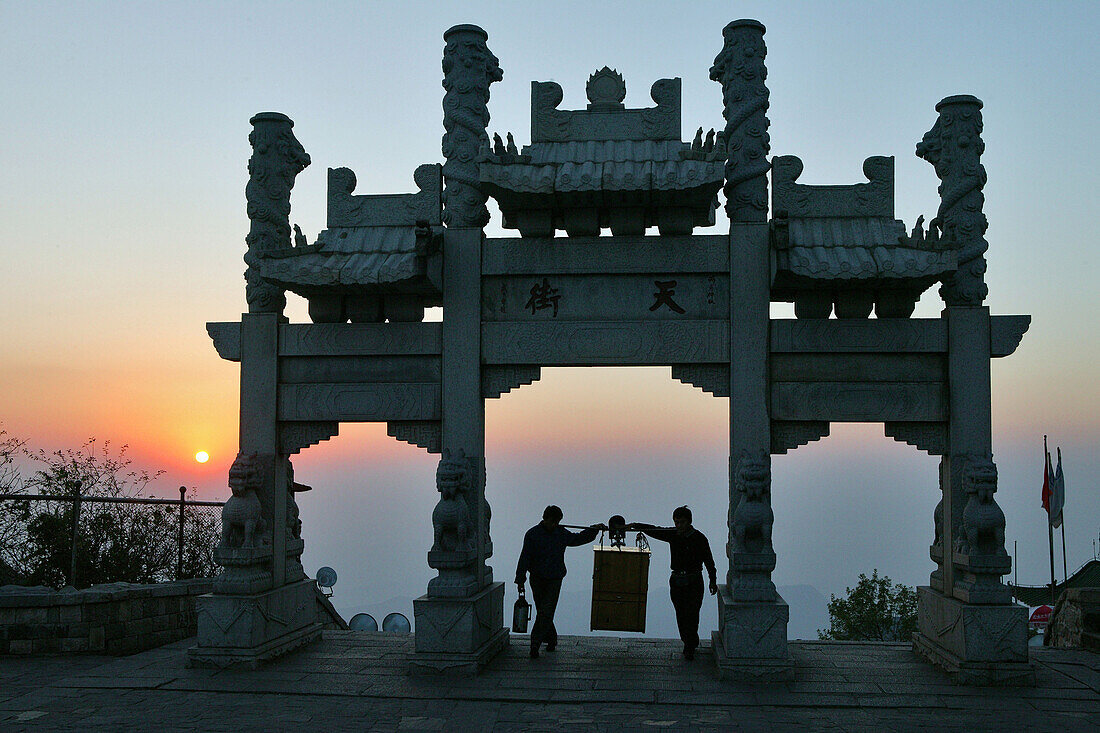 Torbogen am Südlichen Himmelstor im Abendrot, Träger erreichen die Heavenly Street, die Hauptstrasse des Bergdorfes, Taishan, Provinz Shandong, UNESCO Weltkulturerbe, China, Asien