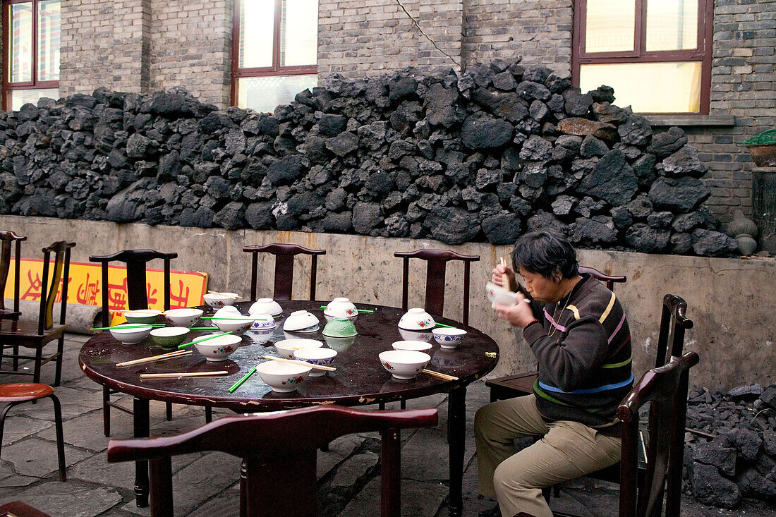 Mann beim Mittagessen, Kohlenlager für die Küche im Hintergrund, Tempelfest zu Ehren Wenshus, Schutzgottheit des Wutai Shan, Xiantong Temple, Taihuai Stadt, Provinz Shanxi, China, Asien