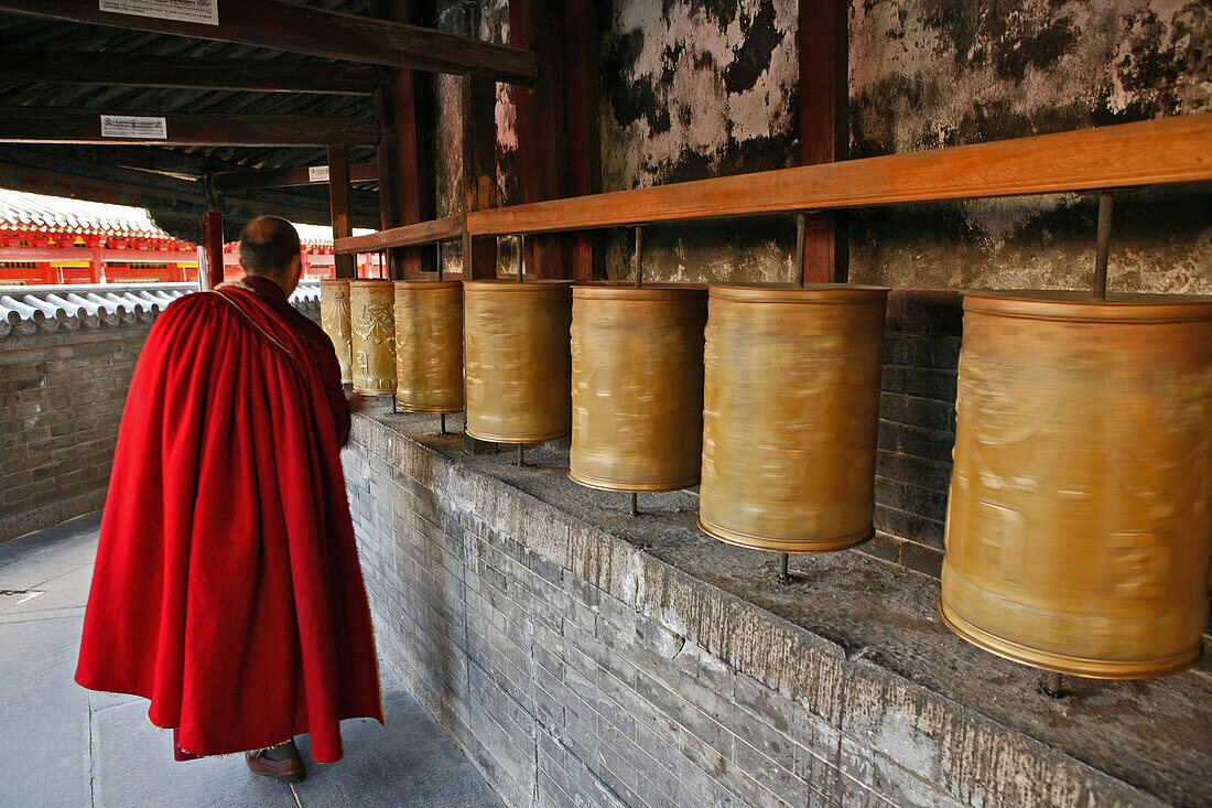 Lama monk turns the prayer wheels at the base of the Great White Pagoda, during the birthday celebrations for Wenshu, Tayuan Monastery, Wutai Shan, Five Terrace Mountain, Buddhist Centre, town of Taihuai, Shanxi province, China
