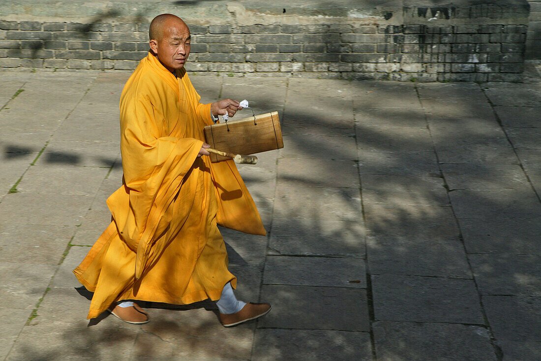 monk in yellow rope calls with a wooden drum for the prayer, during birthday of Wenshu, Wutai Shan, Five Terrace Mountain, Buddhist Centre, town of Taihuai, Shanxi province, China, Asia