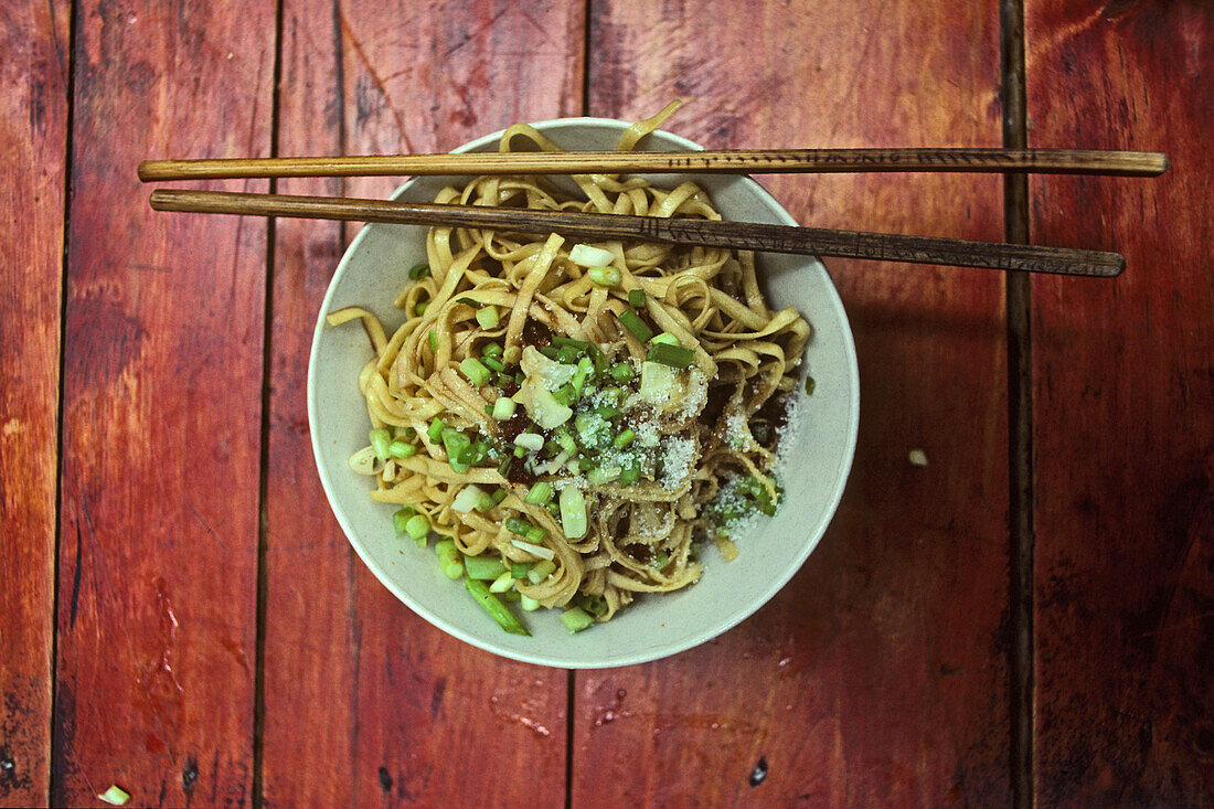 Chinese food, bowl of noodles with chilli, spring onions and sugar on a red tablespringonions, typical street snack in Sichuan, China
