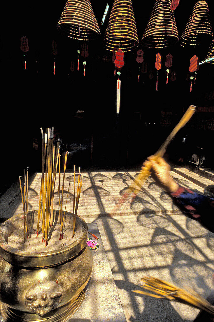 Spiral incense coils hanging from a temple ceiling, Woman lighting an incense stick in the foreground, China
