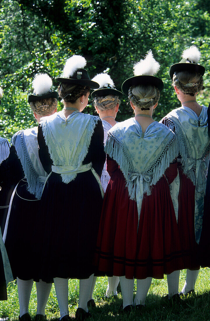 Group of young women in dirndl dresses from the back with traditional hats and eagle down feathers, pilgrimage to Raiten, Schleching, Chiemgau, Upper Bavaria, Bavaria, Germany