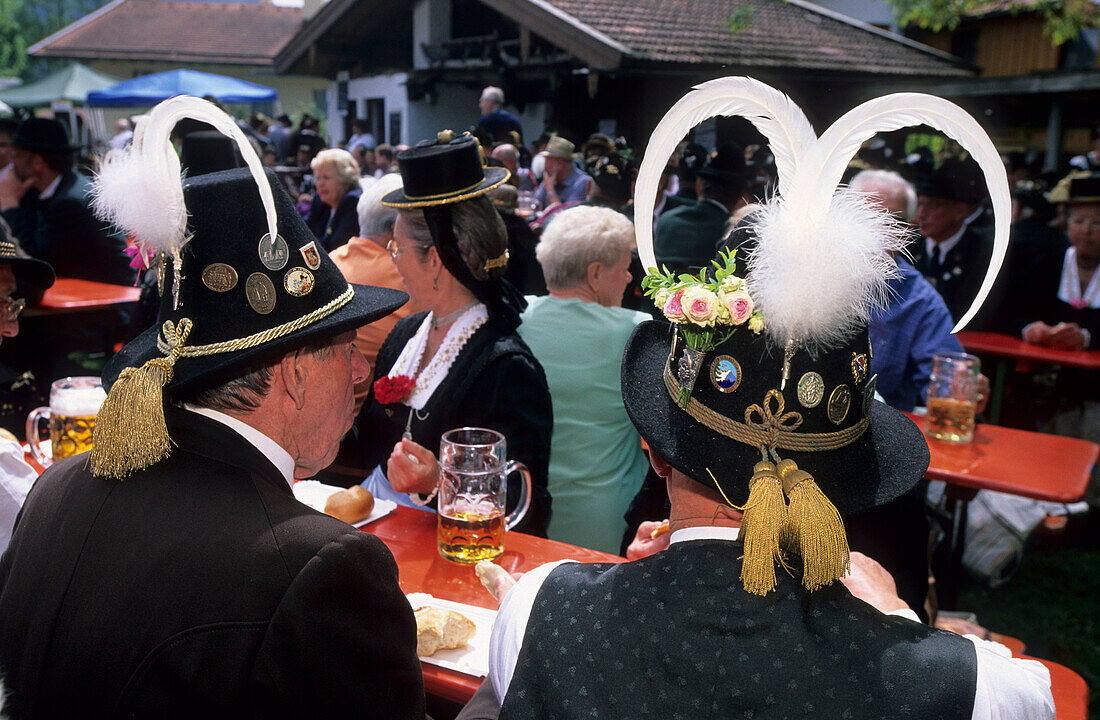 two men in traditional dresses from the backside with traditional hat and feathers, in beer garden, pilgrimage to Raiten, Schleching, Chiemgau, Upper Bavaria, Bavaria, Germany