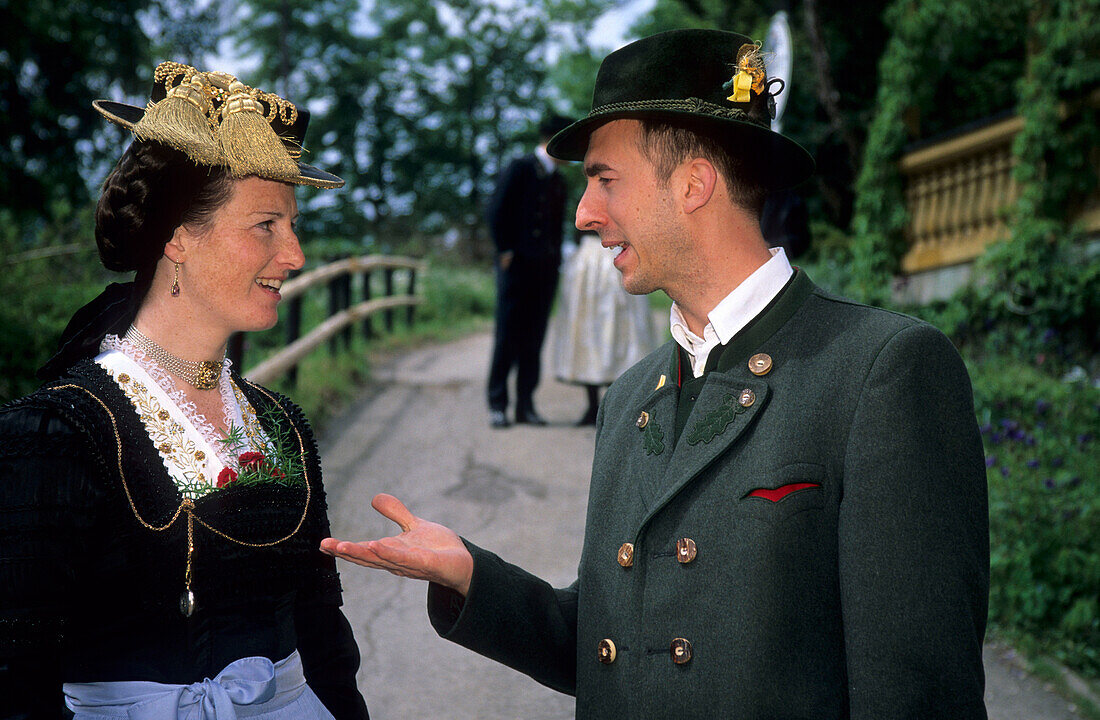Young couple in dirndl dress and traditional dress talking to each other, pilgrimage to Raiten, Schleching, Chiemgau, Upper Bavaria, Bavaria, Germany