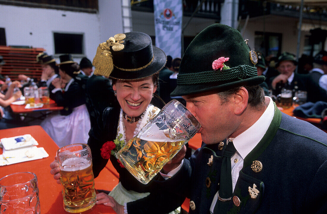 Young couple in dirndl dress and traditional dress, saying cheers in a beer garden, pilgrimage to Raiten, Schleching, Chiemgau, Upper Bavaria, Bavaria, Germany