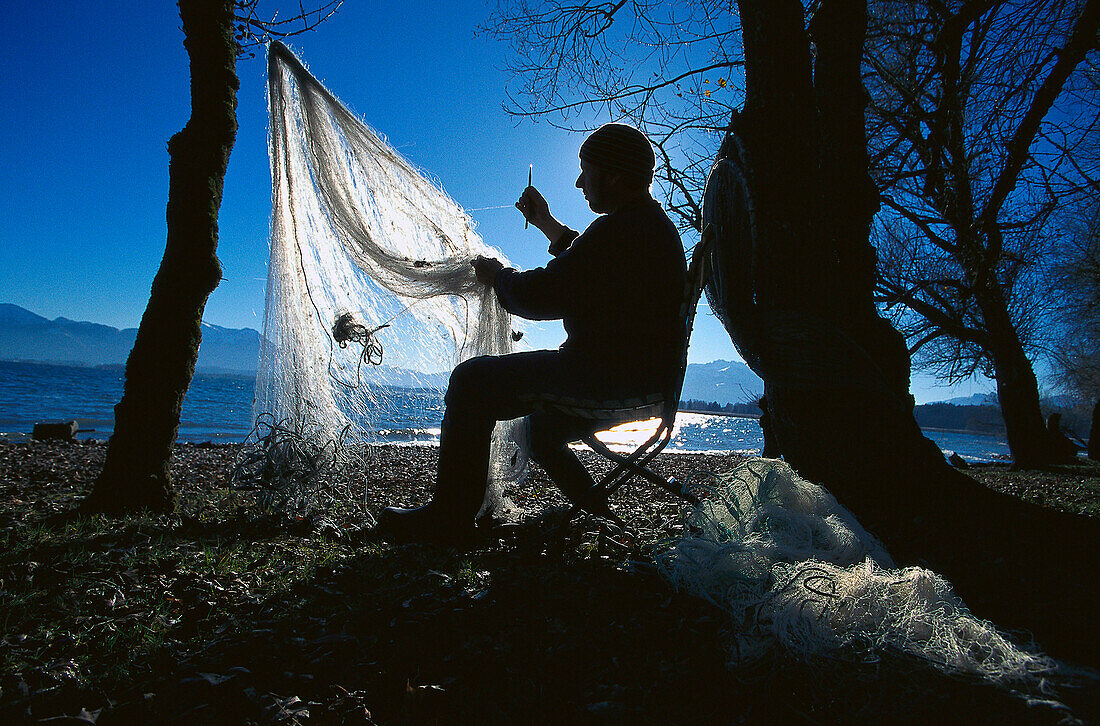 Ein Fischermann repariert sein Fischnetz, Chiemsee, Bayern, Deutschland