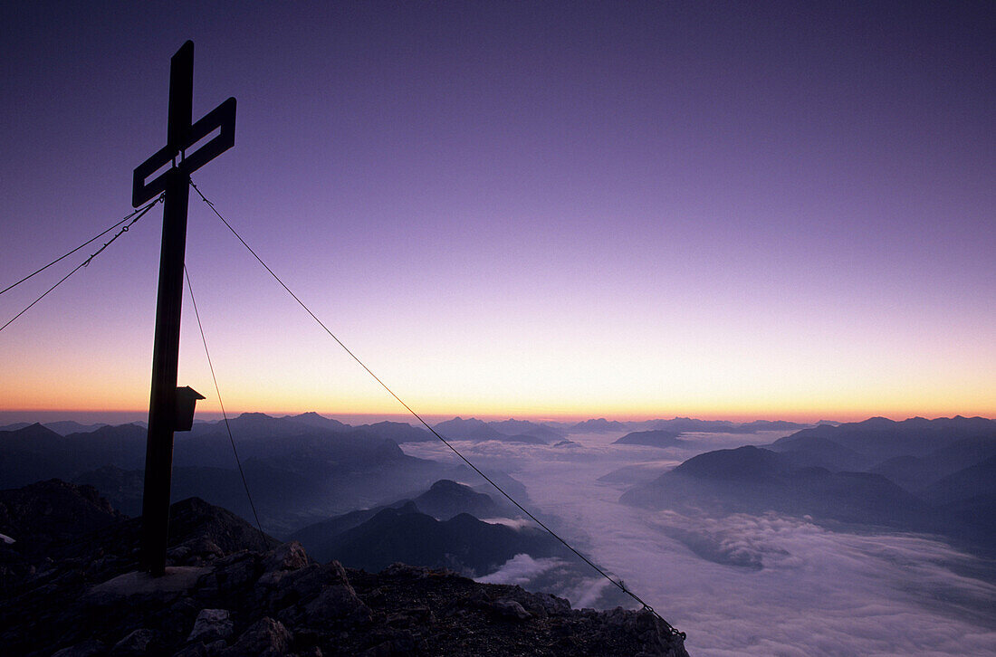 Morgendämmerung am Gipfelkreuz des Grimming mit Blick über das Nebelmeer im Ennstal zum Gesäuse, Dachsteingruppe, Steiermark, Österreich