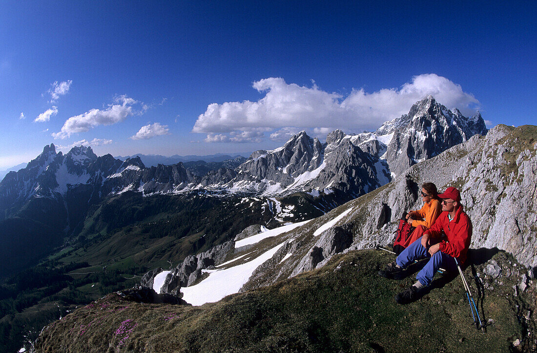 Two hikers resting at Roetelstein with view over to Bischofsmuetze and Torstein, Dachstein mountain range, Salzburg, Austria