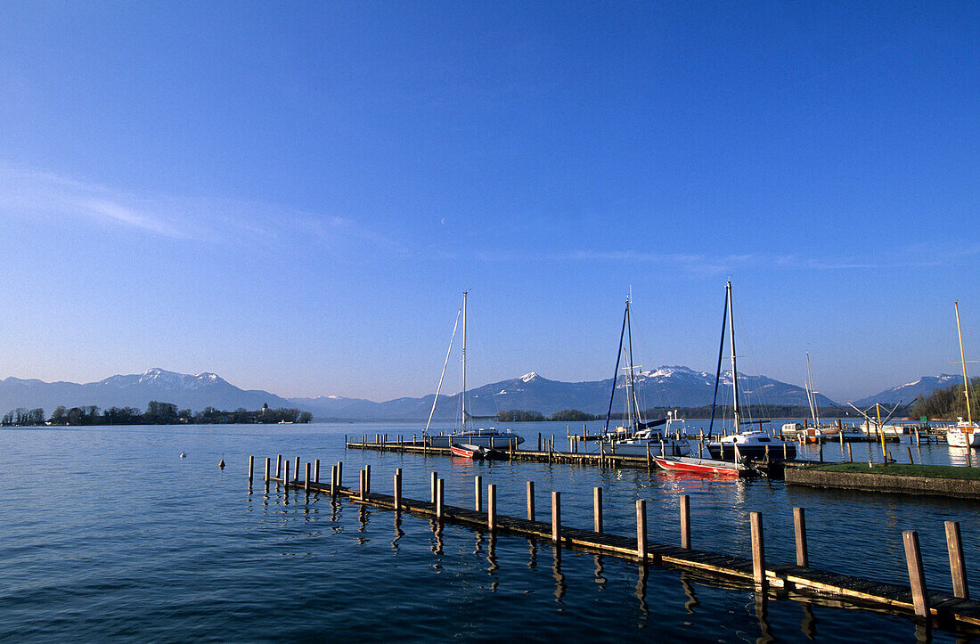 Landing stage and boats in Gstadt at lake Chiemsee with Fraueninsel, Hochgern and Kampenwand in the background, Chiemgau, Upper Bavaria, Bavaria, Germany