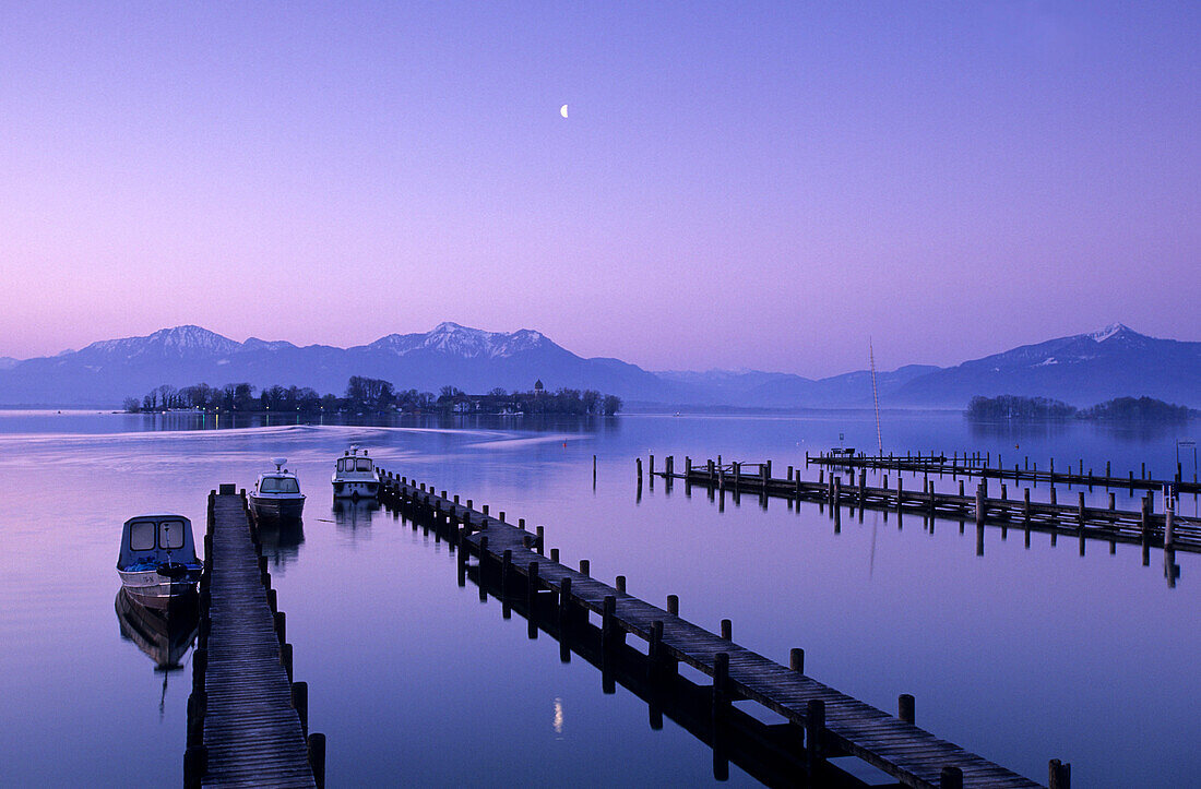Landing stage and boats at dawn in Gstadt at lake Chiemsee with Fraueninsel, Hochplatte, Hochgern and Hochfelln in the background, Chiemgau, Upper Bavaria, Bavaria, Germany