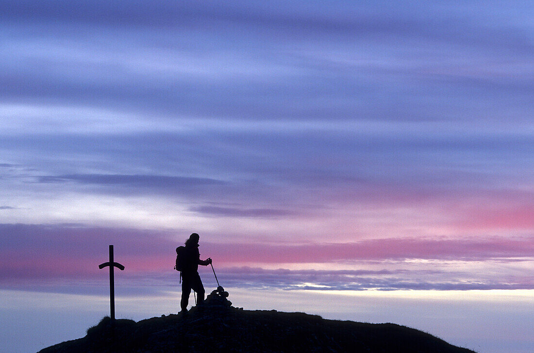 Mountaineer at a cross on the summit with pink clouds, Monte Penna, Pelmo range, Dolomites, Venezia, Italy