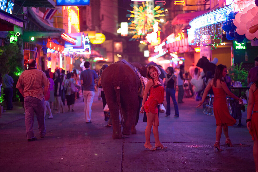 People strolling over Soi Cowboy with bars and nightclubs, red-light district, woman smiling at camera in foreground, Th Sukhumvit, Bangkok, Thailand