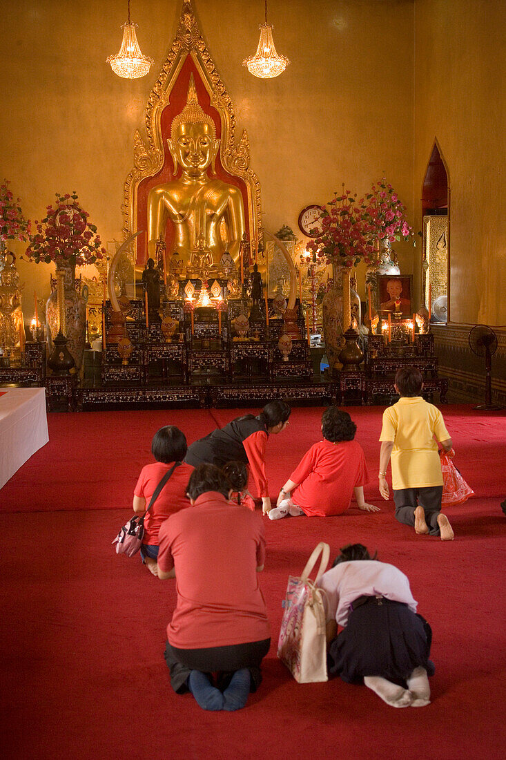 People praying in front of a gilded Buddha statue, Wat Suthat, Bangkok, Thailand