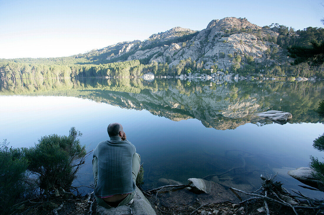 Man sitting on lakeside reservoir lake "barrage de ospedale", Bavella, Southern Corse, France