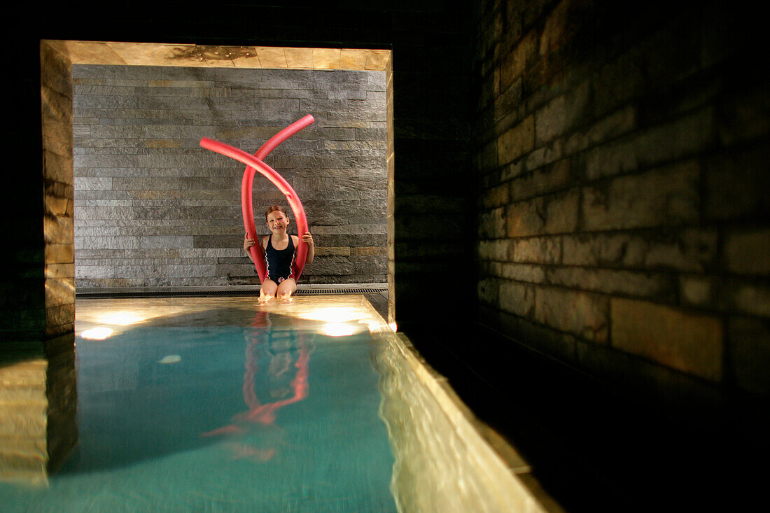 Girl sitting on poolside, holding swimming tubes, Hotel Krallerhof, Leogang, Salzburger Land, Austria