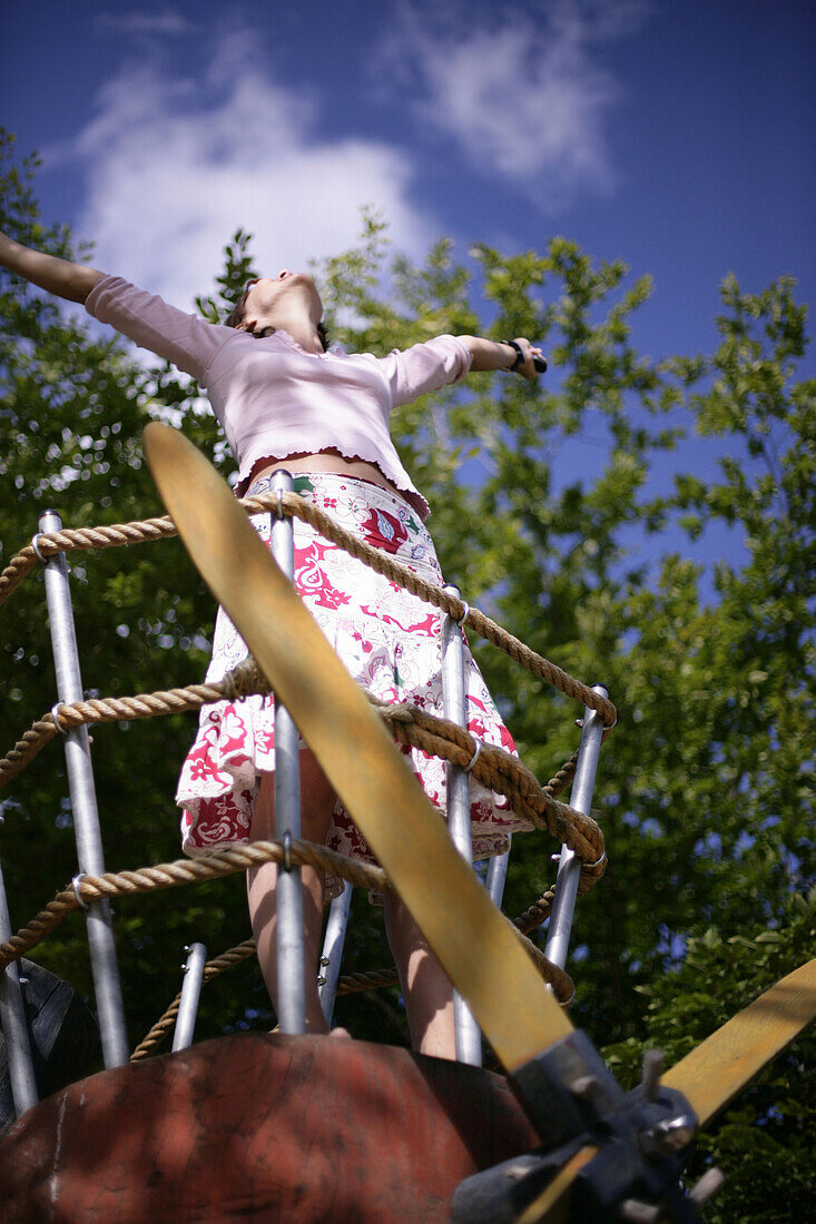 Young woman at playground, arms raised, low angle view