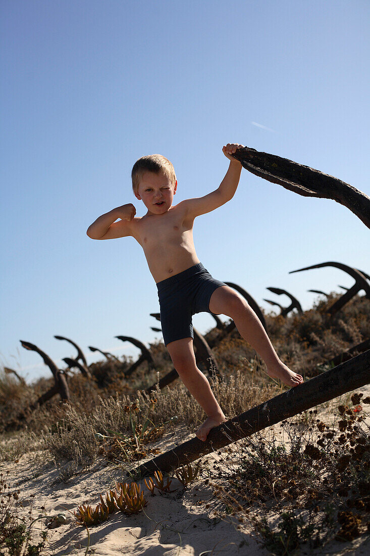 Junge spielt auf einem rostigen Anker am Strand, Ilha de Tavira, Tavira, Algarve, Portugal