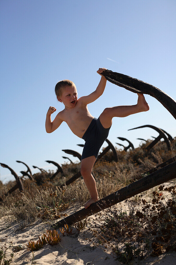 Junge spielt auf einem rostigen Anker am Strand, Ilha de Tavira, Tavira, Algarve, Portugal